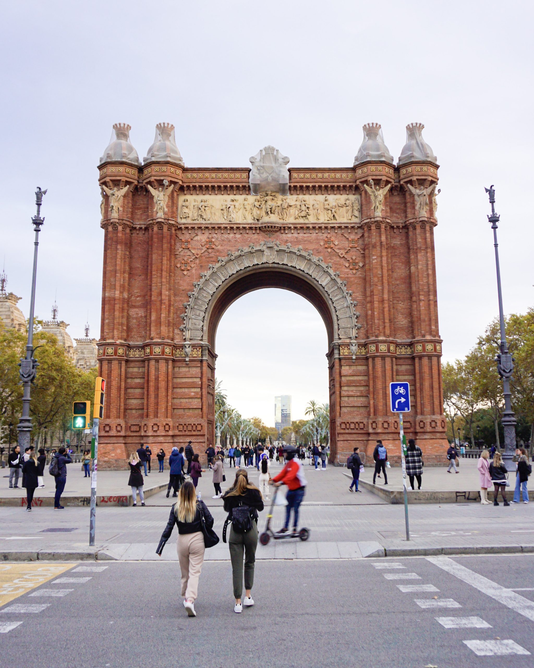 Arc de Triomf seen from the street with pedestrians and scooters.