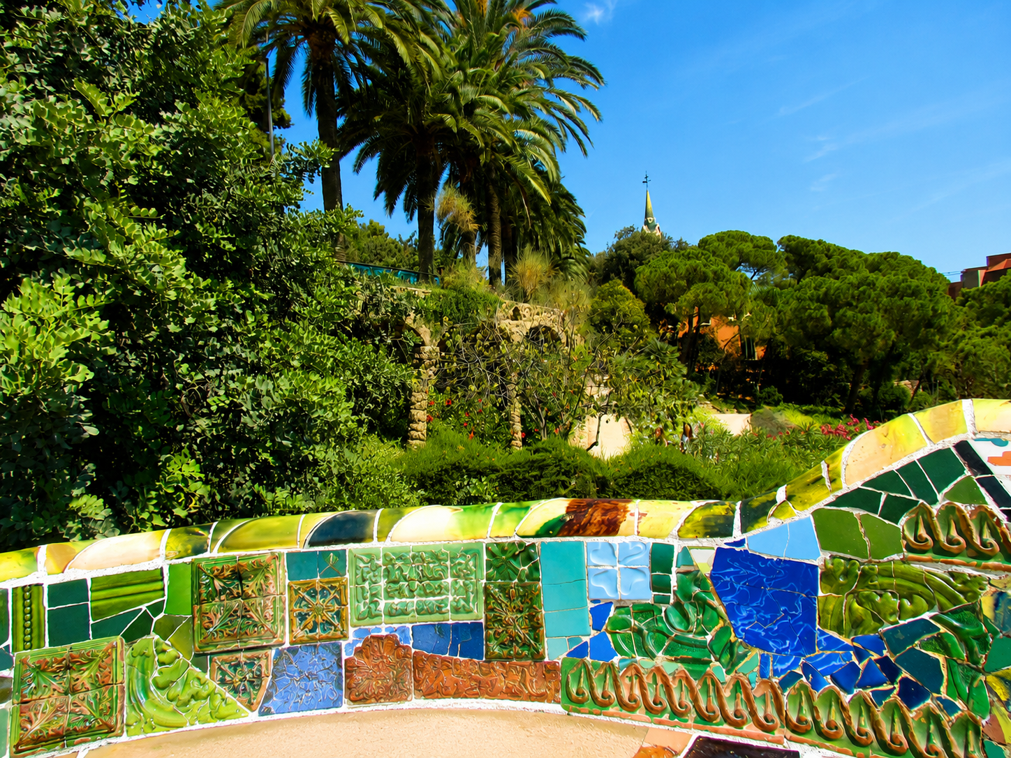Colourful mosaic bench and greenery inside Park Guell.